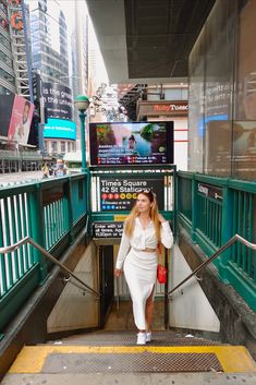 a woman in white is walking down the stairs at a subway station with her hand on her hip