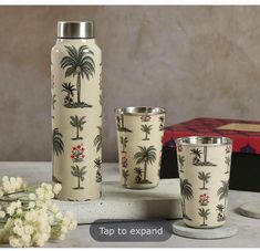 three vases and two cups with palm trees on them are sitting next to each other