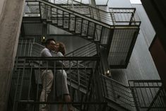 a man and woman standing on top of a metal stair case next to each other