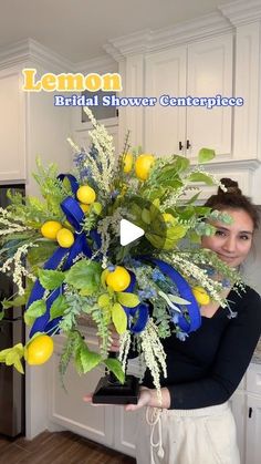 a woman holding a vase with lemons and greenery