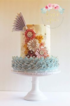 a multi - layered cake decorated with flowers and feathers on a white pedestal in front of a wall