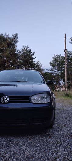 a black car parked on gravel next to trees