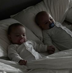 two babies laying in bed next to each other with pacifiers on their mouths