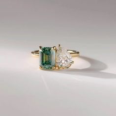 an emerald and diamond ring with two pear shaped diamonds on the side, set in yellow gold