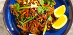 a blue plate topped with noodles and veggies next to lemon wedges on top of a table