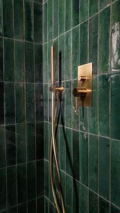 a green tiled shower with brass fixtures and hand held faucet in the corner