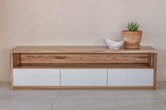 a wooden shelf with two white drawers and a potted plant on top, against a beige wall