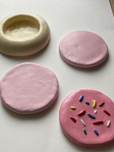 three pink and one white doughnuts with sprinkles next to each other