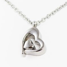 Stainless steel cremation necklace with a heart shaped pendant. A solid heart sits safety inside a larger heart outline, a very comforting and elegant design. The ash is added through the twist top (see picture). An 18 silver chain is included. This necklace for ashes comes with information and supplies. Engraving available. Not to be submerged in water.Capacity: nominal, less than 1 cubic inch. Dimensions: 1.00H x .75W. Materials: Stainless steel. Double Heart Silver Stainless Steel Necklace, Stainless Steel Heart Necklace For Anniversary, Keepsake Heart Pendant Necklace In Stainless Steel, Stainless Steel Heart Pendant Necklace For Keepsake, Heart Pendant Necklace In Stainless Steel For Keepsake, Stainless Steel Heart Pendant Necklace For Anniversary, Silver Double Heart Stainless Steel Necklace, Stainless Steel Double Heart Necklace For Anniversary, Silver Stainless Steel Double Heart Necklace