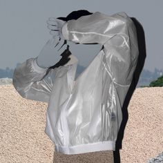 a person wearing a silver jacket and holding their hands up to their head while standing in front of a stone wall