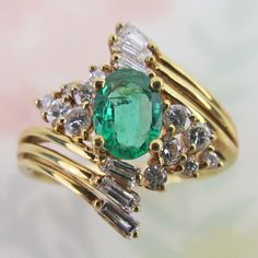 Natural diamond clusters and yellow gold swirls surround a lovely bright green emerald gem on this vintage 14k yellow gold ring. The gemstones are bright, vivid and lively. The round faceted diamonds are mounted in tiered settings. The diamond baguettes are set at the end of each yellow gold swirl, giving the ring lots of visual sparkle and movement. The ring was finished with a linear gallery and a sturdy thick gold shank band.  The oval-faceted emerald is of rich medium green color with visibl Yellow Gold Cocktail Ring, Emerald Gem, Gold Cocktail Ring, Gold Cocktail, Green Emerald, Baguette Diamond, Vintage Ring, Natural Emerald, Diamond Cluster