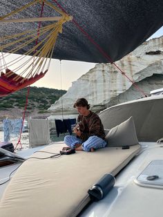 a man sitting on the back of a boat using a cell phone and laptop computer