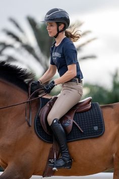 a young woman riding on the back of a brown horse in an equestrian outfit and helmet