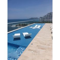 an empty swimming pool with white lounge chairs on the side and ocean in the background