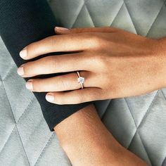 a woman's hand with a diamond ring on top of her finger, resting on a quilted surface