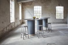 an empty room with three stools and a round table in the center surrounded by windows