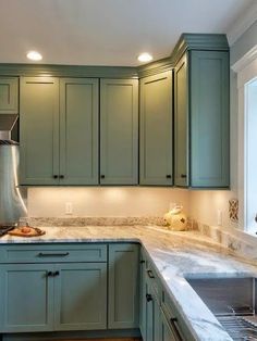 a kitchen with green cabinets and marble counter tops