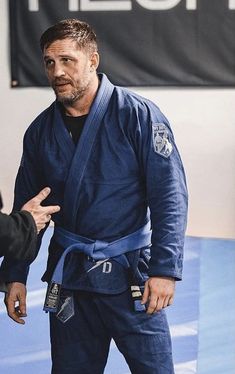 a man standing next to another man in a blue kimono and black belted uniform