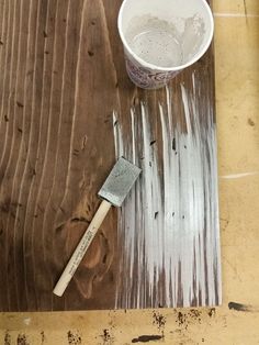 a paintbrush sitting on top of a wooden table next to a bucket and brush