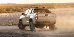 a silver chevrolet truck driving down a dirt road in the middle of the desert with dust coming from its tires