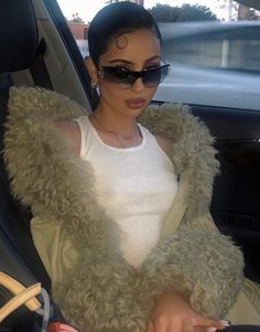 a woman sitting in the back seat of a car wearing sunglasses and a furry coat