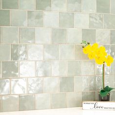 a vase with yellow flowers in it sitting on a counter next to a tile wall