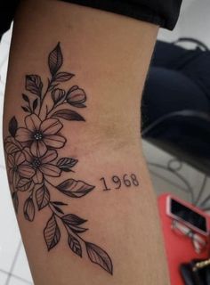 a woman's leg with flowers on it and the date tattooed in black ink