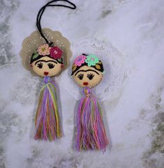 two dolls are hanging on a lace doily with tassels and flowers in their hair