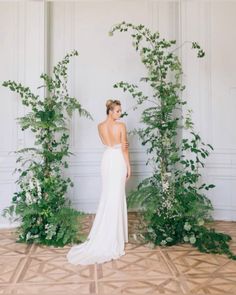 a woman in a wedding dress standing next to greenery