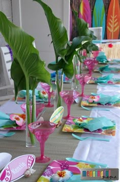 the table is set with pink and blue plates, napkins, and green plants