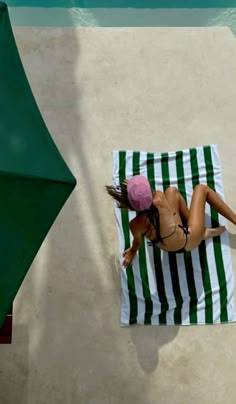 a woman laying on top of a green and white striped towel next to an umbrella