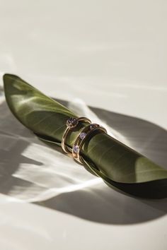 two gold wedding rings sitting on top of a green leaf