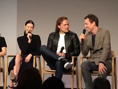 three people sitting in chairs talking to each other while one person holds a microphone up