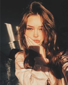 a woman with long brown hair and blue eyes posing for a photo in the sun