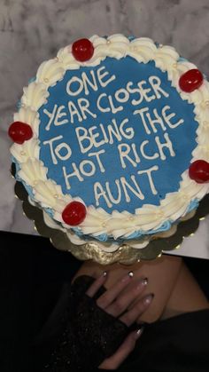 a woman holding up a cake that says one year closer to being the hot rich adult