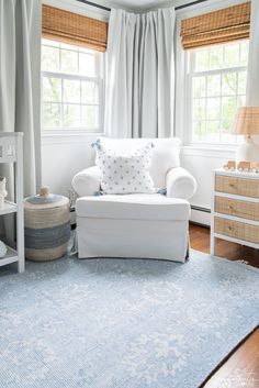 a living room with white furniture and blue rugs on the floor, windows in the background