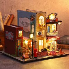 a doll house made out of books and other items on a tray with lights in front of it