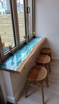 three wooden stools sit in front of a window with an ocean scene painted on it