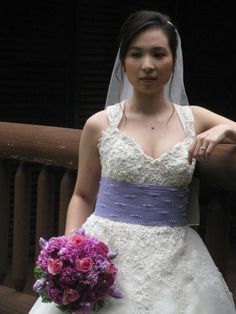 a woman in a wedding dress standing on a balcony holding a purple and white bouquet