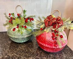 two glass vases with red flowers and greenery in them sitting on a counter