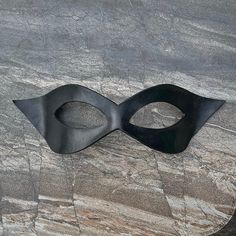 This little leather half mask is so versatile, it can work for a wide range of costumes  from bandit to Zorro, to superhero, or supervillain! MEASUREMENTS + MATERIALS ✭ Materal: tooling leather, dye, paint, sealant, and quality ribbon ties. ✭ Measures approximately 8.5" wide x 3" high at the highest and widest points ✭ Ties with gorgeous and durable stretch lace ribbon straps (included). This well made domino/half mask was cut and shaped from premium tooling leather. It has been dyed and painted in opaque black. The color is sealed with a protective top coat. The size is just right for most adults, and the shape is flattering on men and women alike. The last few photos show this mask design in other color variations, and being worn by real live humans. These images are included to help con Black Superhero Masquerade Mask, Novelty Black Masks For Halloween, Black Novelty Costume Masks, Adjustable Black Fantasy Mask, Leather Half Mask, Comicon Cosplay, Paint Sealant, Superhero Cosplay, Half Mask