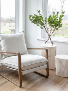 a white chair sitting in front of a window next to a wooden table with a potted plant on it