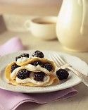 a white plate topped with crepes covered in blackberries next to a fork