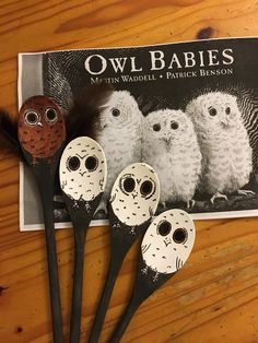 three owl baby spoons sitting on top of a wooden table next to two feathers