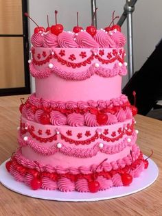 a three tiered pink cake with cherries on the top and red icing