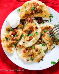 a white plate topped with dumplings covered in cheese and bacon next to a fork