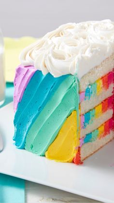 a slice of cake with rainbow frosting on a plate next to a glass of milk