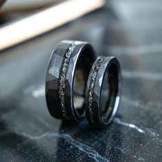 two wedding bands with black diamonds on them sitting on top of a table next to each other