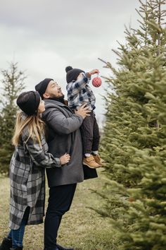 a man and woman are standing in front of a christmas tree with their son on his shoulders