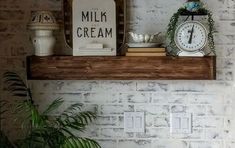 a clock and some plants on a shelf in a room with white brick wallpaper